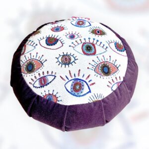 Cette image représente un zafu coussin de méditation petit modèle avec le contour violet et une assise avec des yeux protecteurs